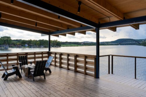 Lakeside boathouse with Kebony wood decking, open-beam roof structure, and cable railing overlooking the water, using durable modified wood supplied by TimberTown.