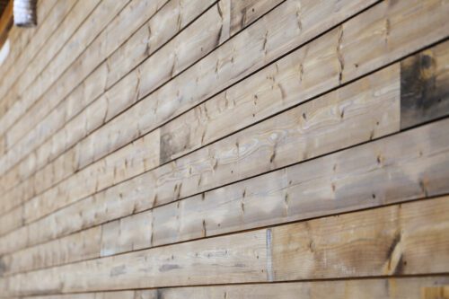Close-up of Kebony wood cladding showing the natural weathered grain, warm tone variations, and smooth modified-wood texture.